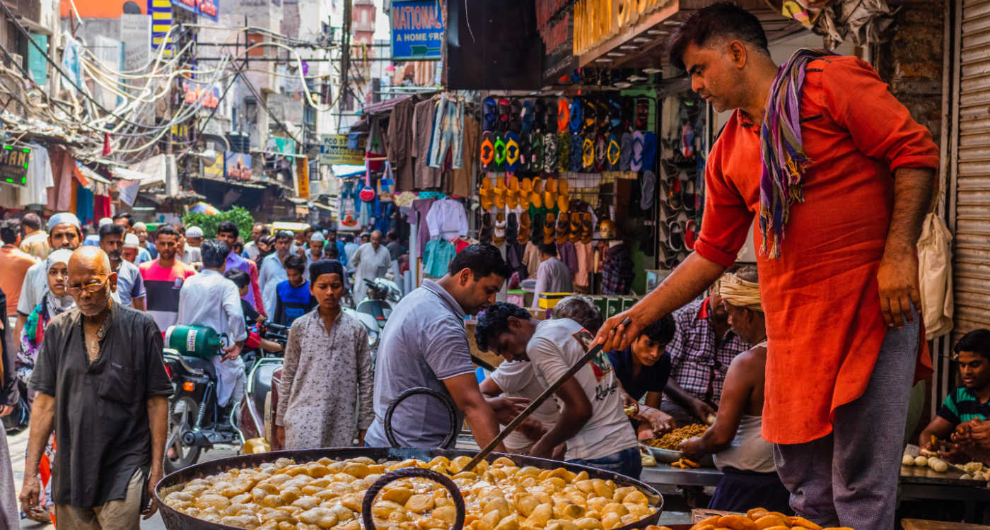 A man cooking a large pan of street snacks on a busy street in Delhi [Photo: Shutterstock]