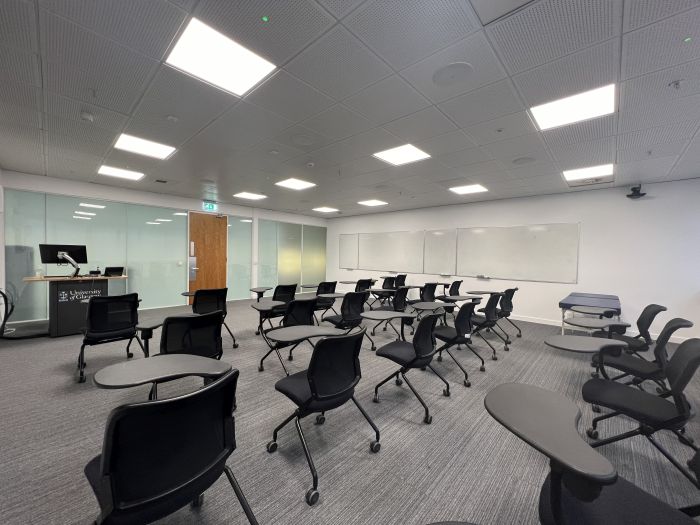 Flat floored teaching room with tablet chairs, clinical skills bed, whiteboards, lectern, and PC.
