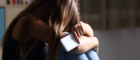 A young person sitting on the floor with her head on her knees while holding a mobile phone