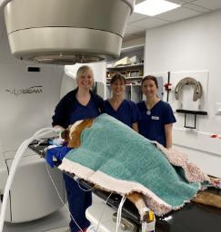 Image of a linear accelerator with Levi the dog under a blanket with three veterinary nurses
