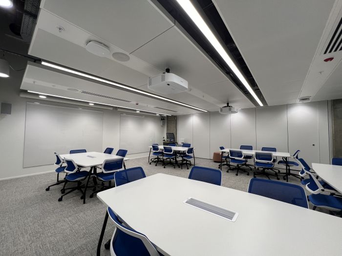 Flat floored teaching room with tables and chairs, projectors, whiteboards, lectern, and PC.