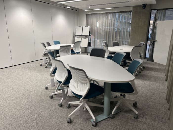 Flat floored teaching room with tables and chairs, and moveable whiteboards.