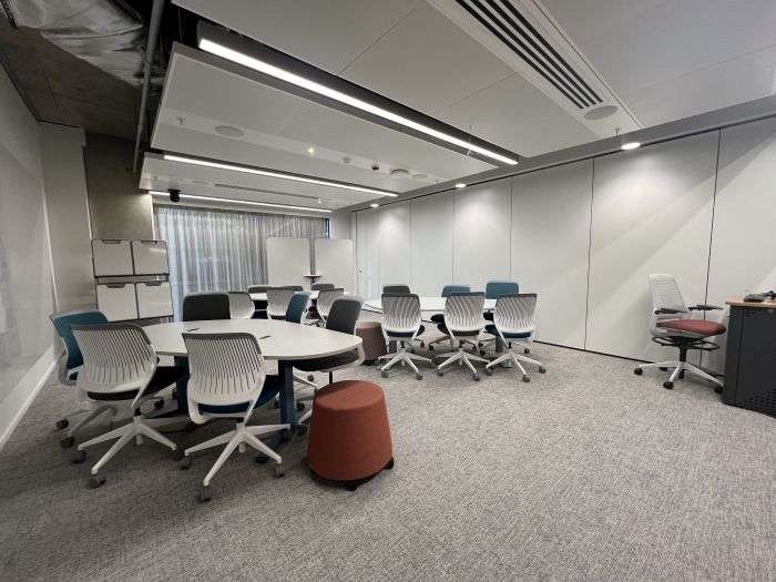Flat floored teaching room with tables, chairs and stools, moveable whiteboards, lectern, and lecturer's chair.
