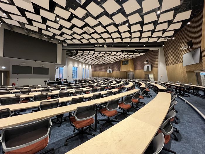 Lecture theatre with workbenches and chairs in semi-circular rows, large screens of varying sizes, and lecterns.