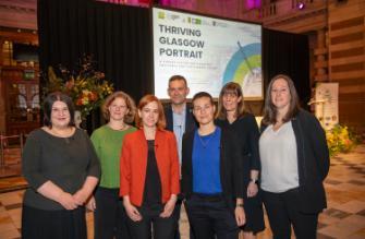 The full panel standing in front of the stage at the Thriving Glasgow Portrait launch event at Kelvingrove Museum.