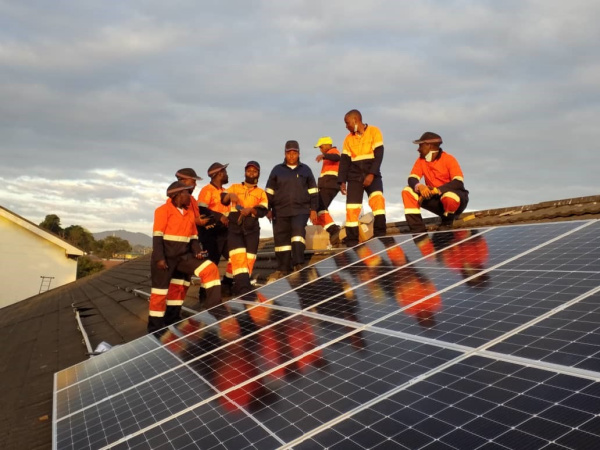 A group of engineers pose next to solar panels they have installed on the roof of the lab