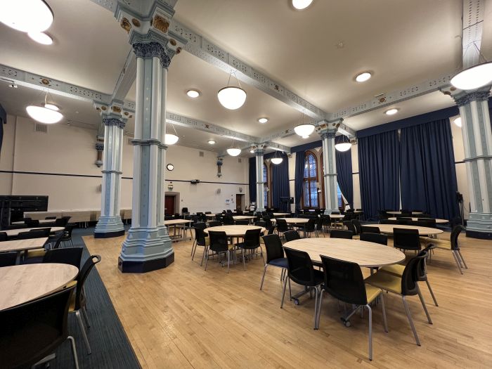 Flat floored hall with tables and chairs in groups, and video monitors.