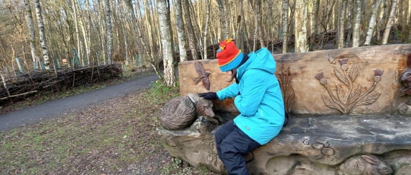 A person pats the head of a carved fox on a bench on a winter's day