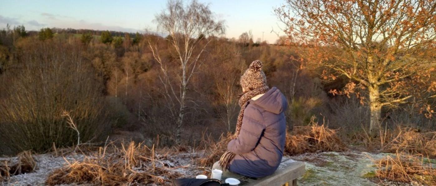 A person sits on a bench with a flask of coffee on a winter's day