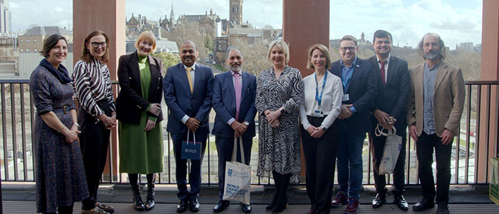 Group photo of University of Glasgow staff and visitors - Consul General of India and the Consul and Head of Chancery, with a view of the University of Glasgow tower in the background
