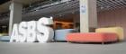 Students in the atrium of the Adam Smith Business School & Postgraduate Taught Hub walking by large ASBS letters