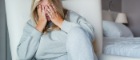 Woman sitting on bed covering her eyes, looking stressed