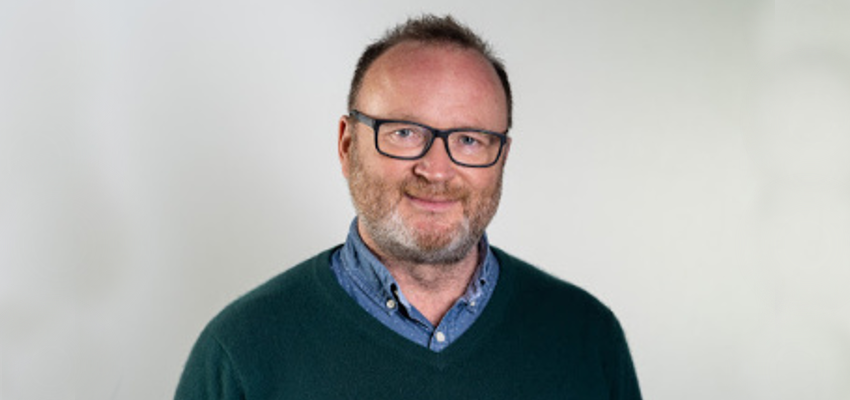 A head and shoulders profile shot of Professor Mike Barrett stood in front of a plain, white background