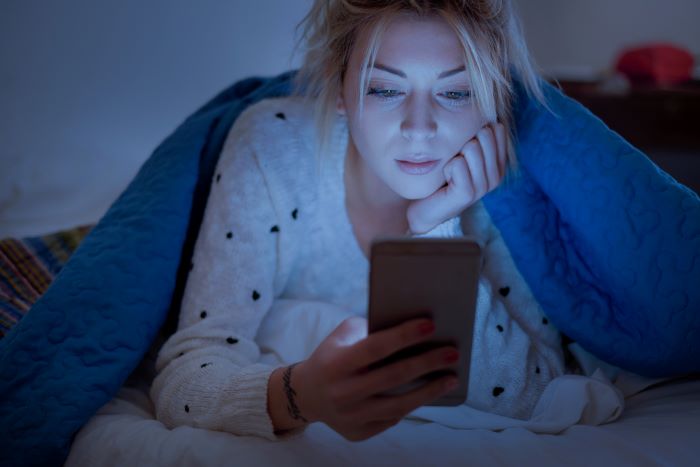 A young woman using her mobile before going to bed