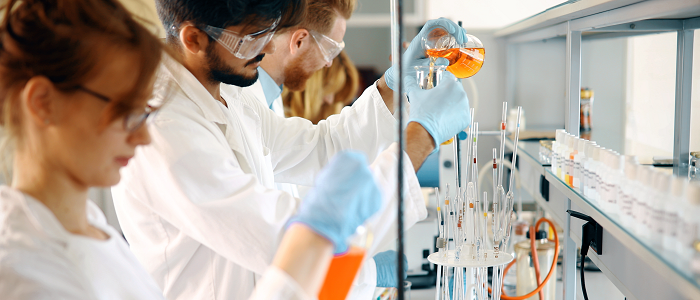 Students standing in laboratory wearing white lab coats and protective goggles