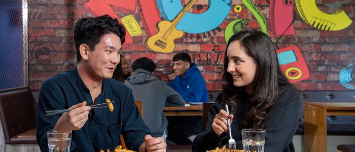 two students eating food in the students union, they are smiling and chatting