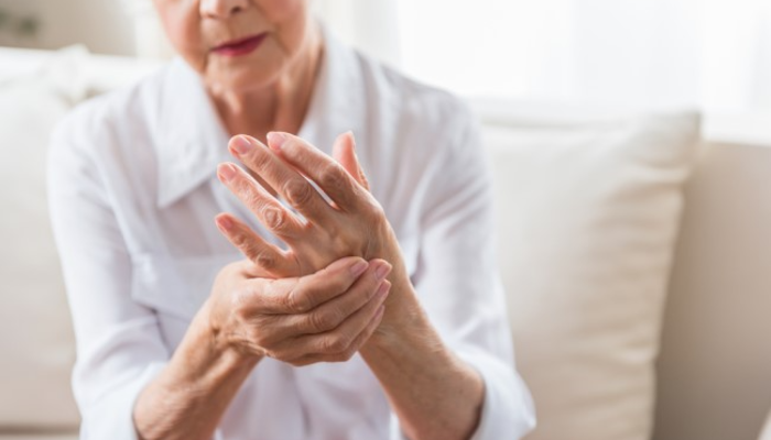 An elderly arthritis patient holding one hand with the other in a display of a flare-up