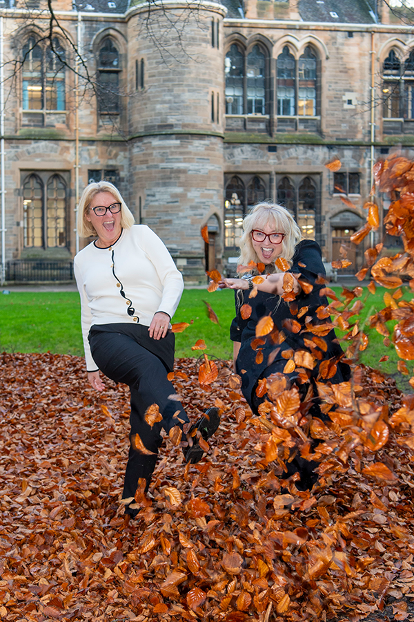 Two women laughing and kicking autumnal leaves towards the camera