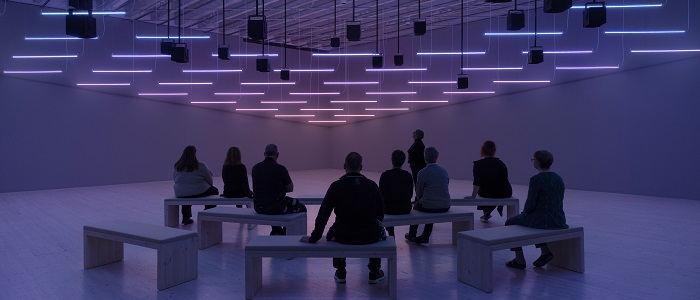 An image of people sitting in a light filled exhibition