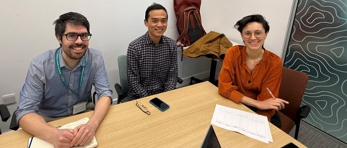 Three researchers sitting behind a table smiling to the camera.