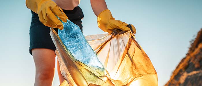 Earth day. A female activist puts a plastic bottle in a garbage bag. Close-up. The concept of environmental conservation and coastal zone cleaning.