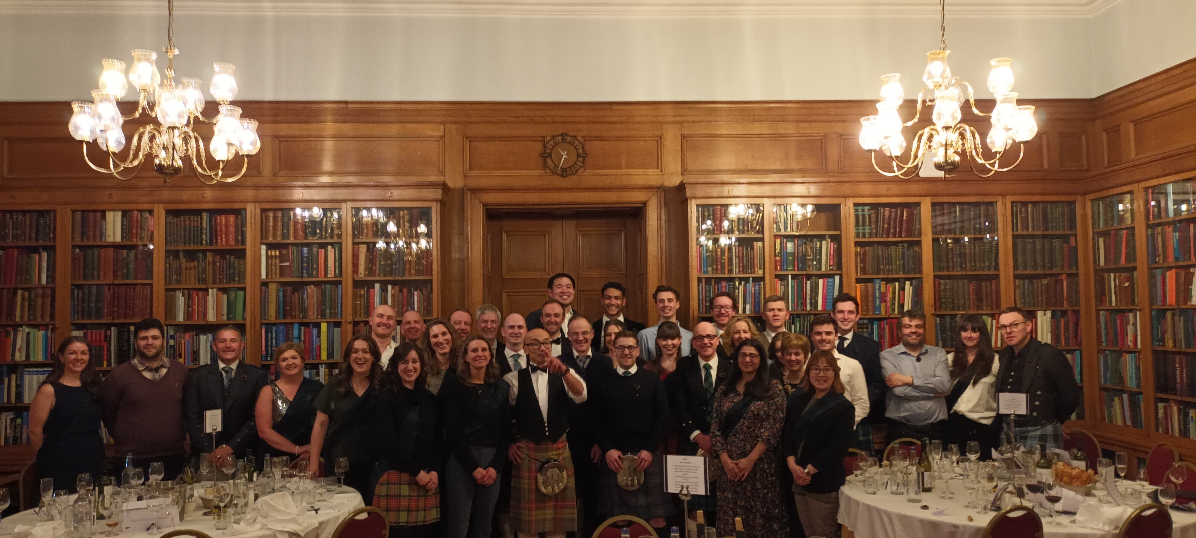 A gathering of Crohn's Futures Meeting attendees stood in a group shot facing the camera in formal attire,, including kilts, at the associated Burns Supper