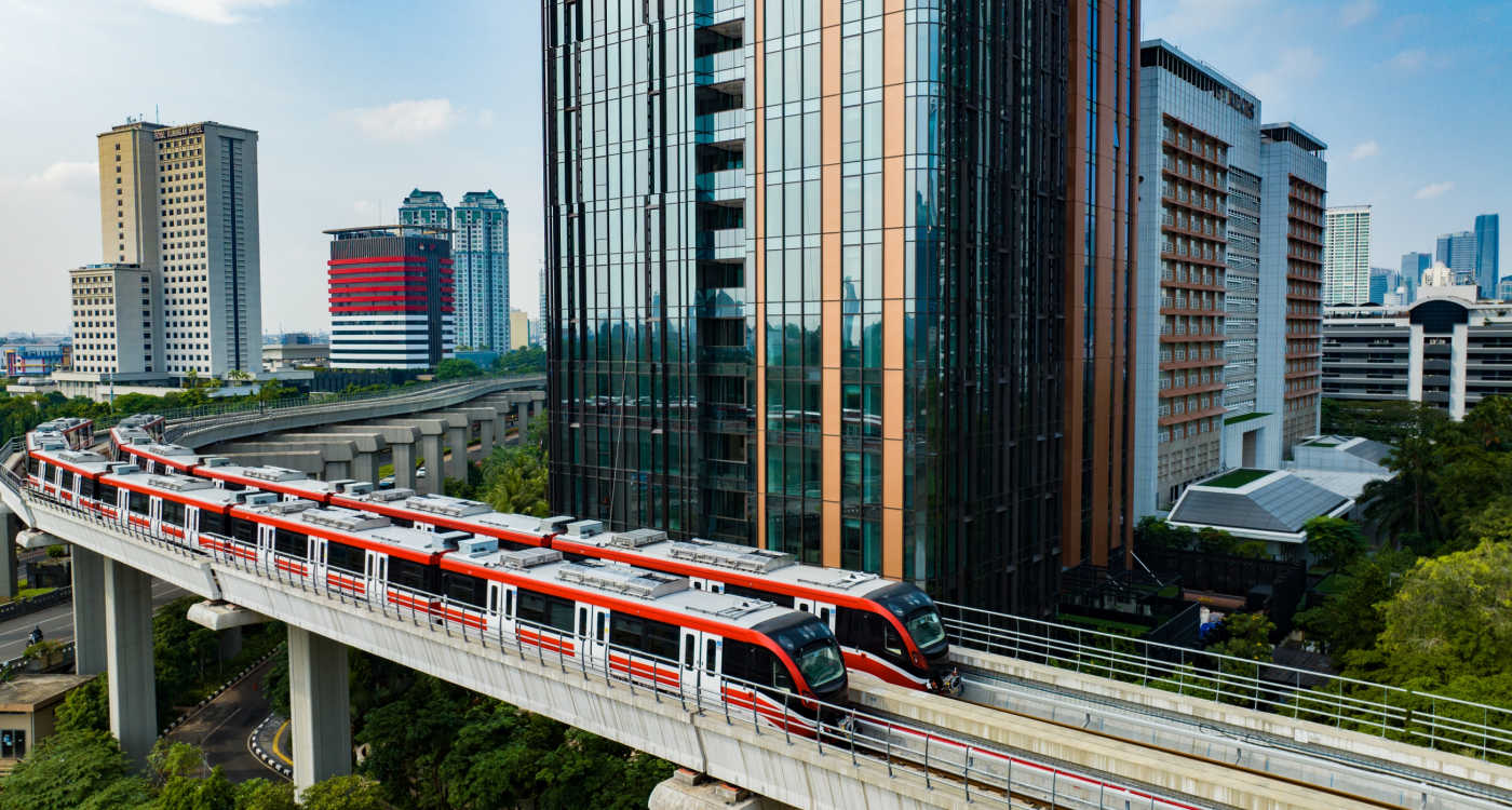 Trains on a raised track going past a tall building in Jakarta