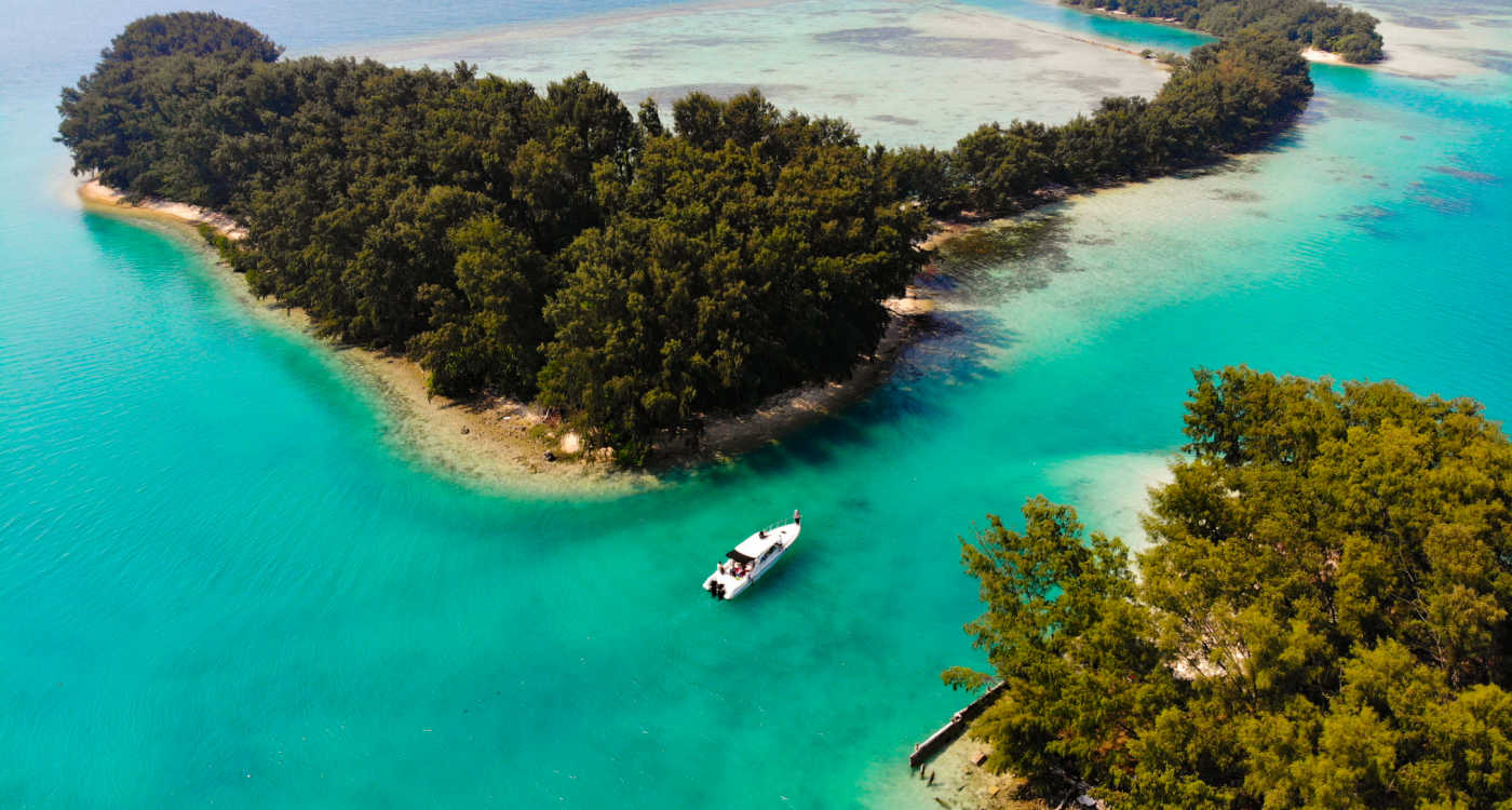 Two tropical islands with turquoise sea with a boat sailing between then at Island Strait, Thousand Islands