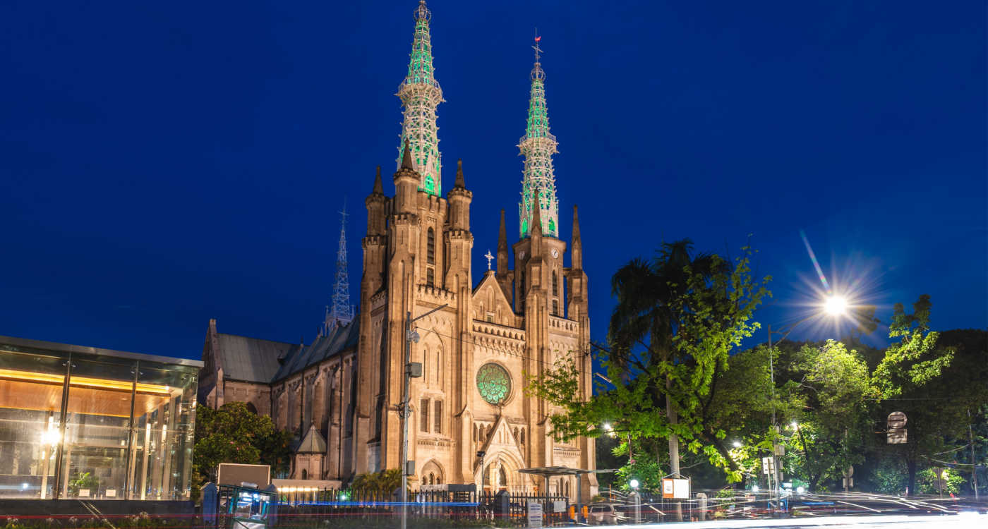 Exterior of Jakarta Cathedral with two tall towers, lit up at night