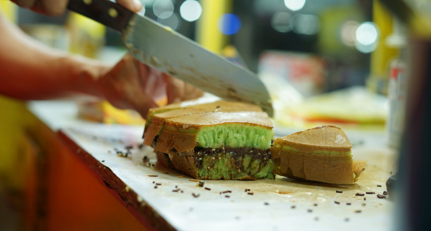 Martabak Manis or Indonesian Sweet Giant Pancake, green tea flavour with cheddar cheese being sliced in half - the sponge is green