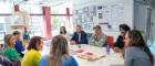 A group of people sitting around the table in Byres Hub with an exhibition wall behind them