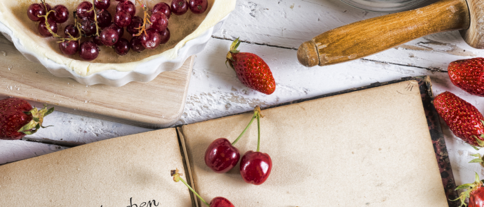 Recipe book with cherries and berries on a white wooden table