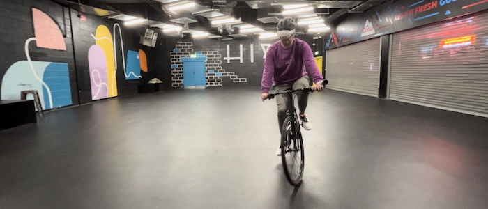 A cyclist rides indoors wearing an AR headset