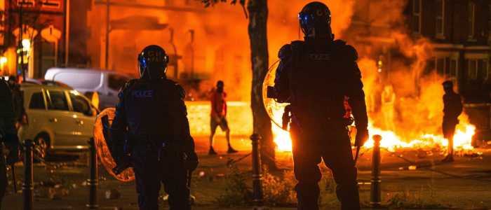 Car on fire at night with police in riot gear