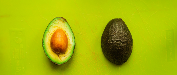 Two avocado halves on a green background, one shows the seed, the other is face down