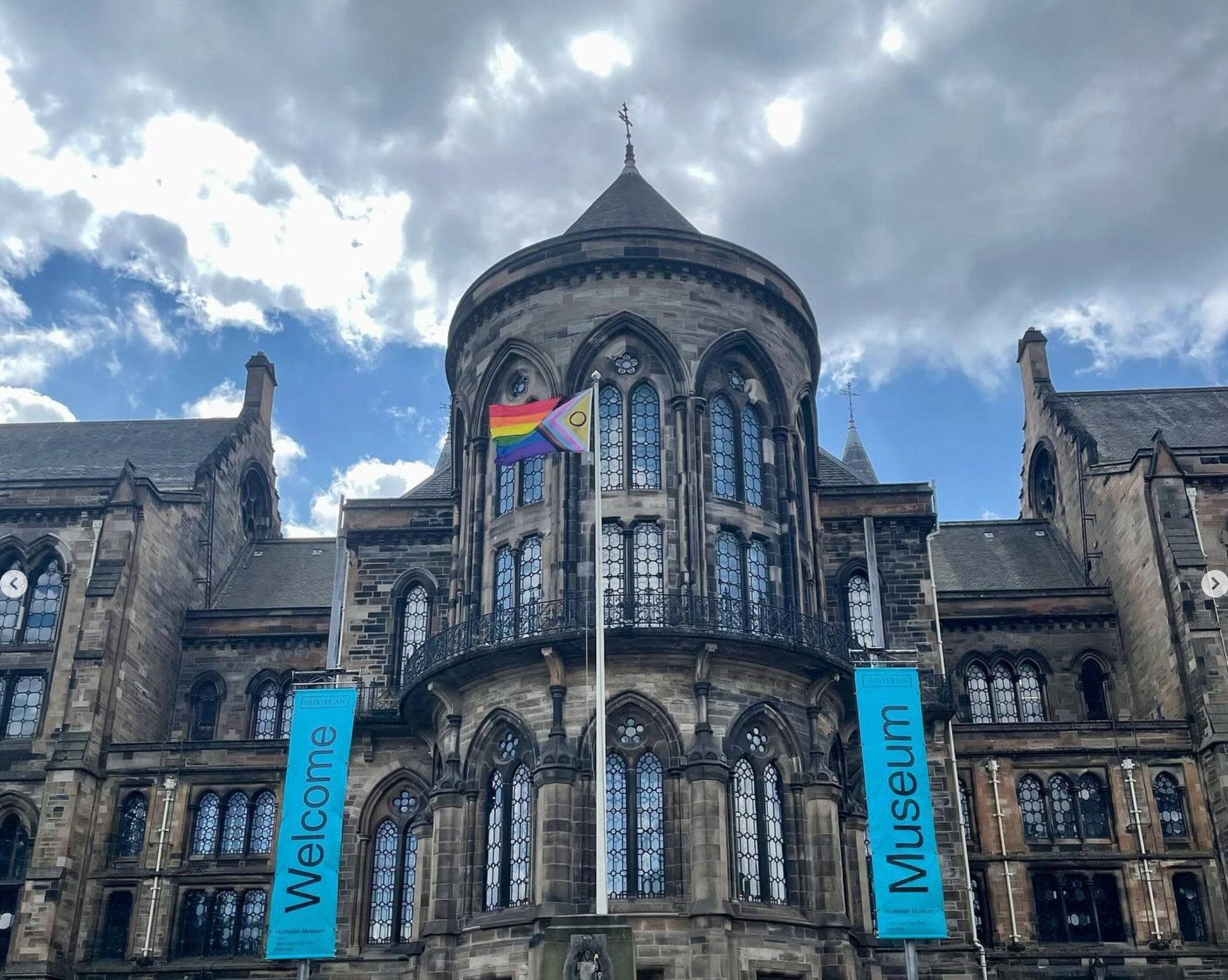 a progressive pride flag flies in front of the University's main building