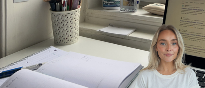 Open notebook on a desk next to laptop and pot of pens with headshot of a smiling woman