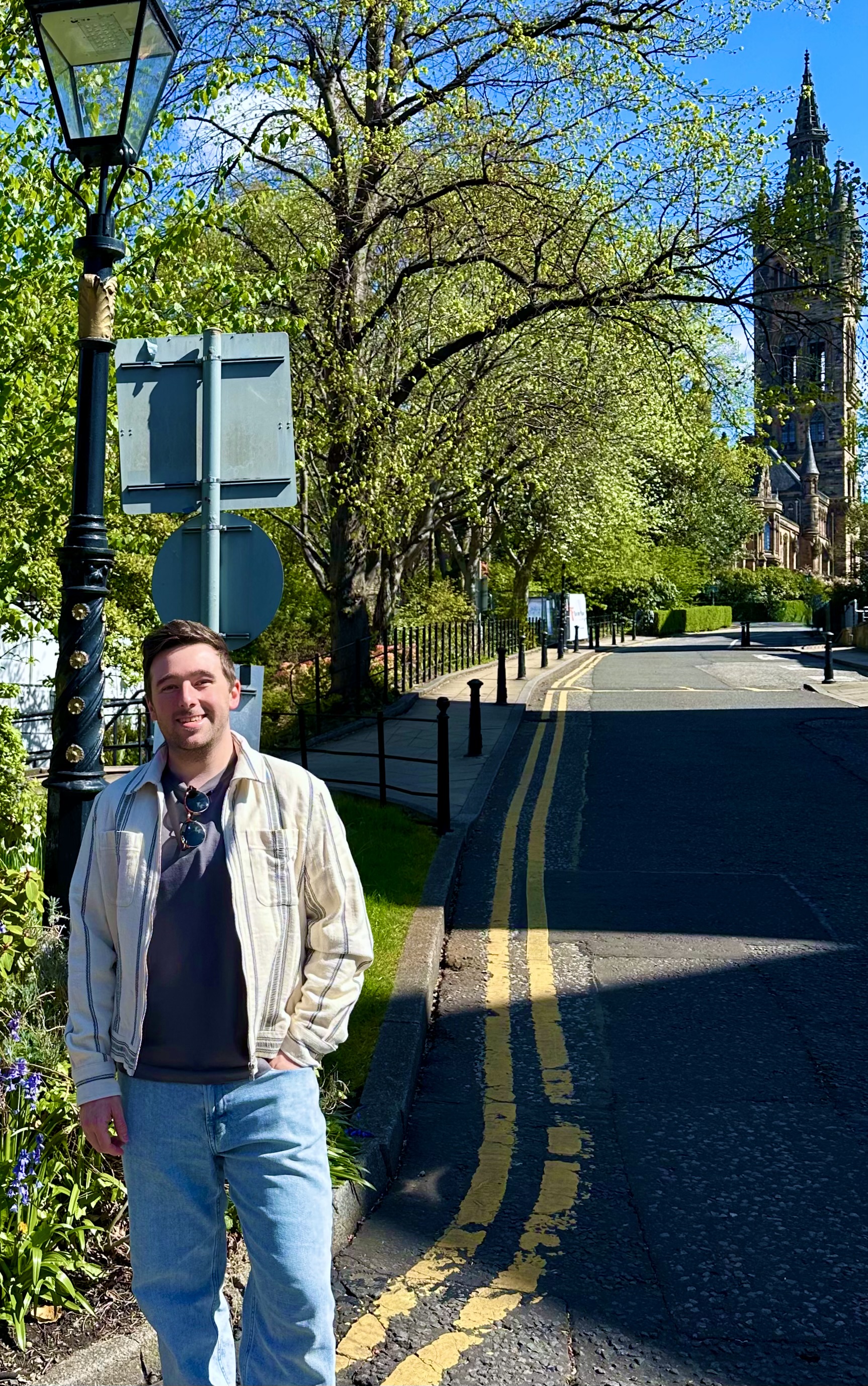 An image of me, standing under a tree on a sunny day, with the Gilbert Scott Building Tower behind.