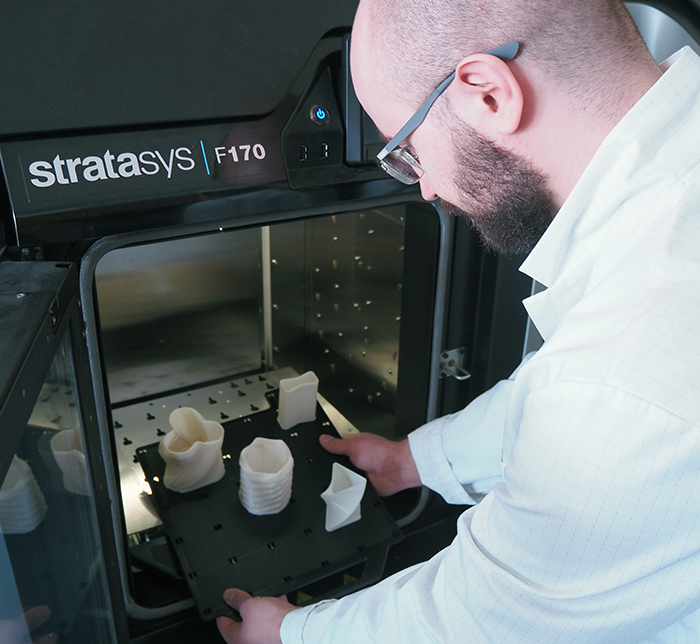 Maember of CAD-Graphics team removing a finished print from a 3D printer.