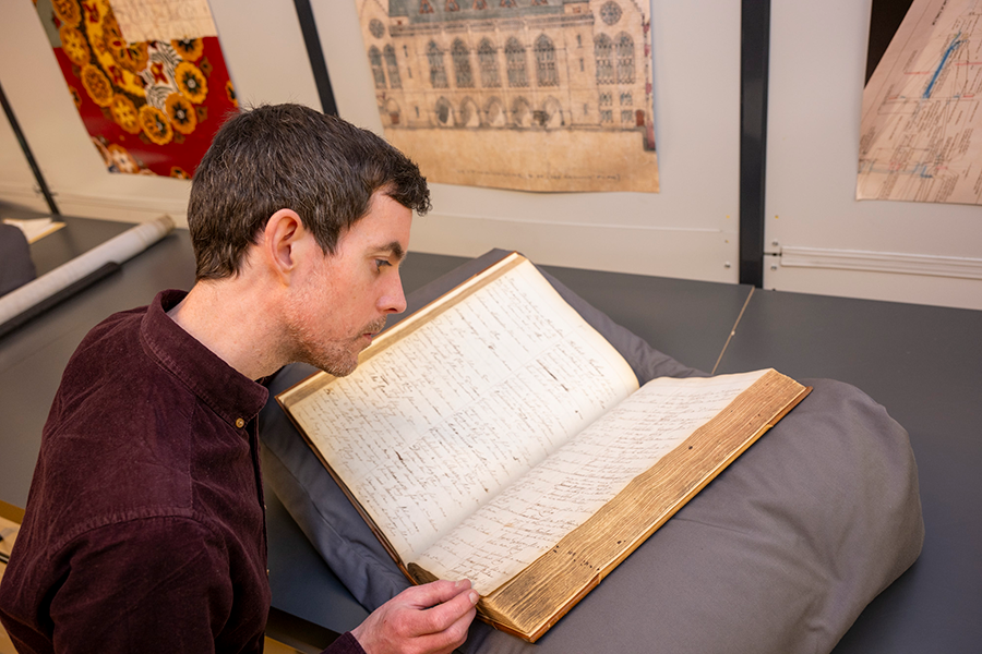 A photo from over the shoulder of Michael Gallagher reading a book in the Archives
