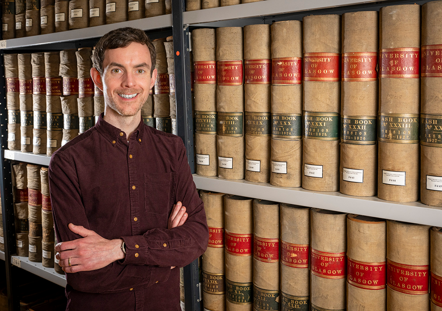 Michael Gallagher leaning against a shelf of archived books in the archives