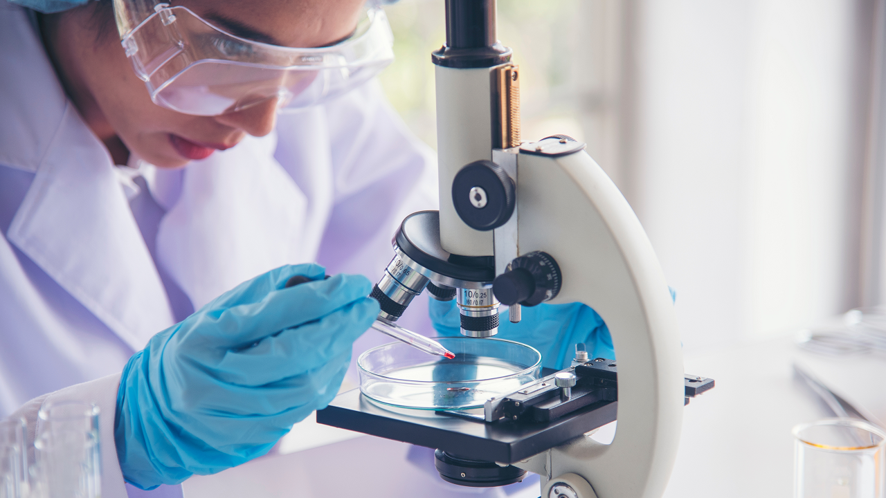 Lab technician with blue gloves looking at microscope