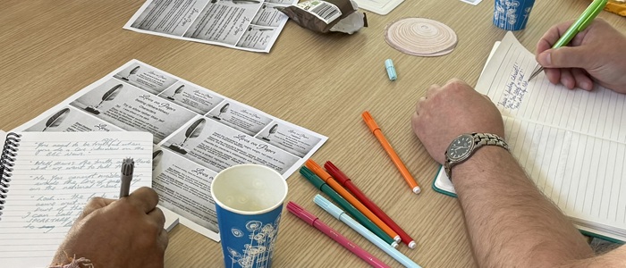 A table with people writing on paper, pencils, and paper coffee cups.