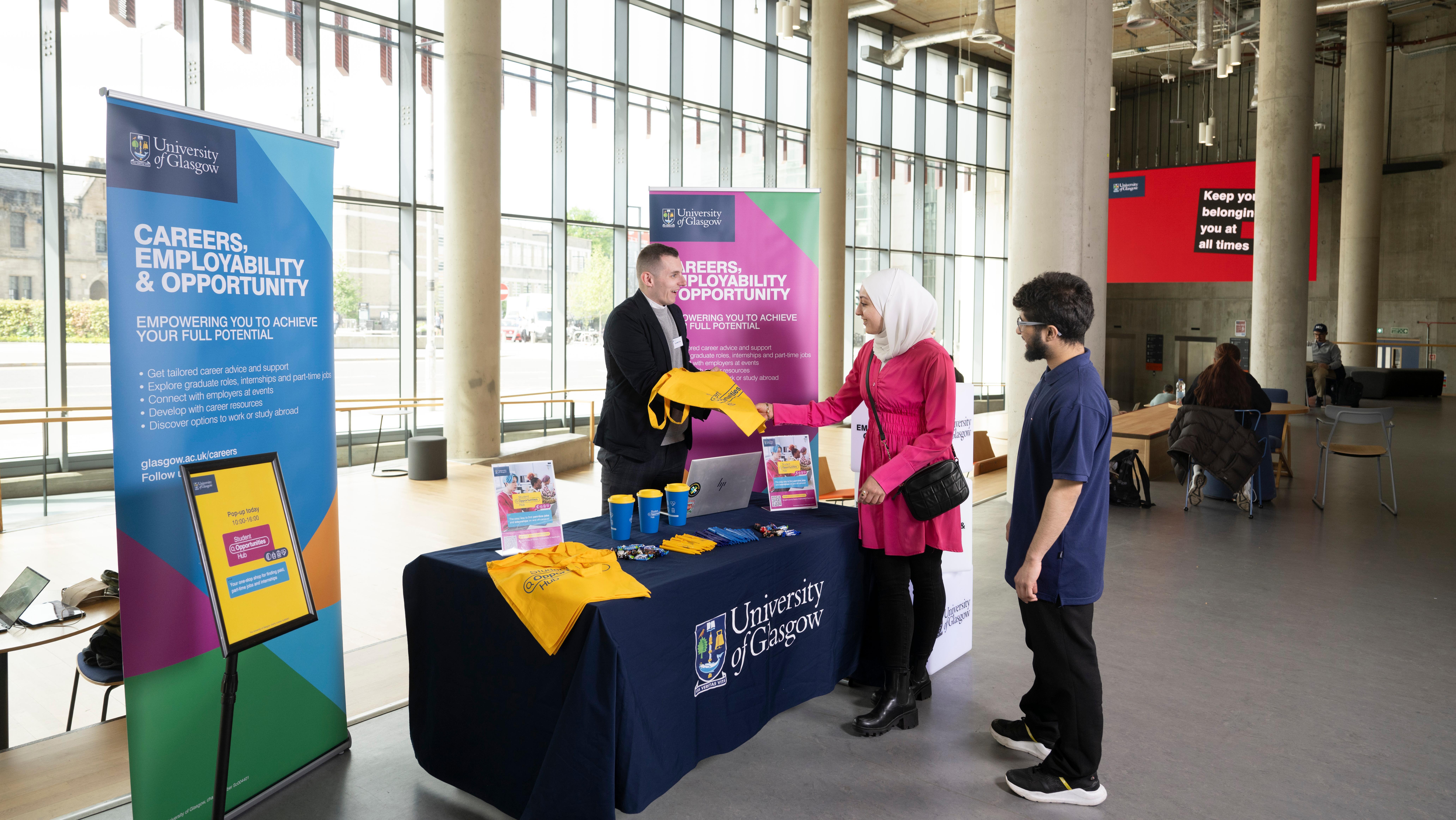 An employer talking to two students at a promotional pop-up stand in the James McCune Smith Building