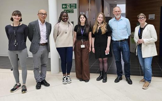 A group of staff and PGR students stood together in a row facing the camera at the PGR Poster Day