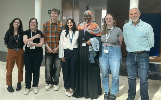 A group of staff and PGR students stood together in a row facing the camera at the PGR Poster Day