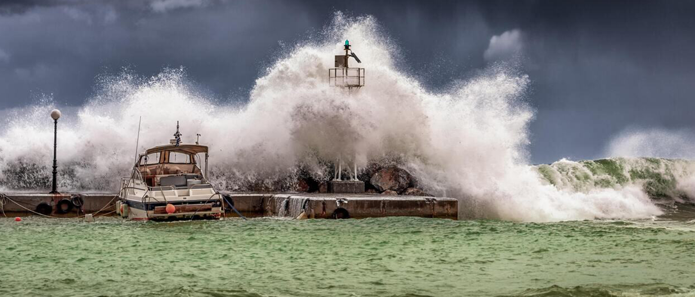 A wvae breaking against a pier with a lighthouse on it