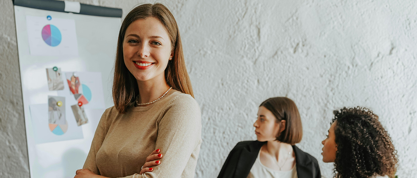 2 women looking at a diagrom on a board with a woman in the foreground smiling at the camera