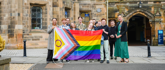 A group of people smiling for a photo holding the progress pride flag
