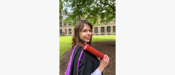 Woman standing in graduation gown with graduation scroll looking over her shoulder